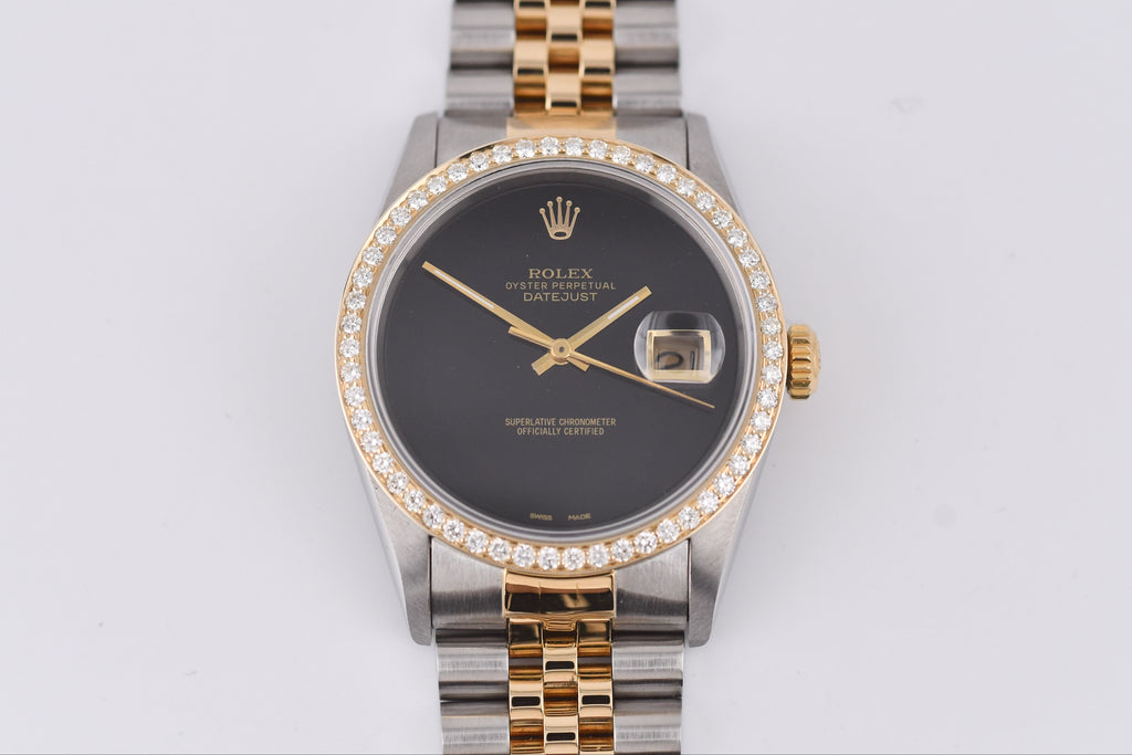 Luxury watch with a dark face and gold and silver band on a light gray background
