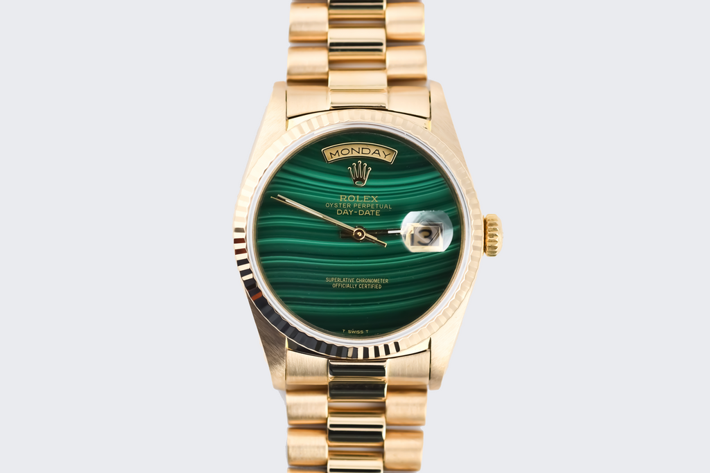 Gold watch with a green face on a light gray background