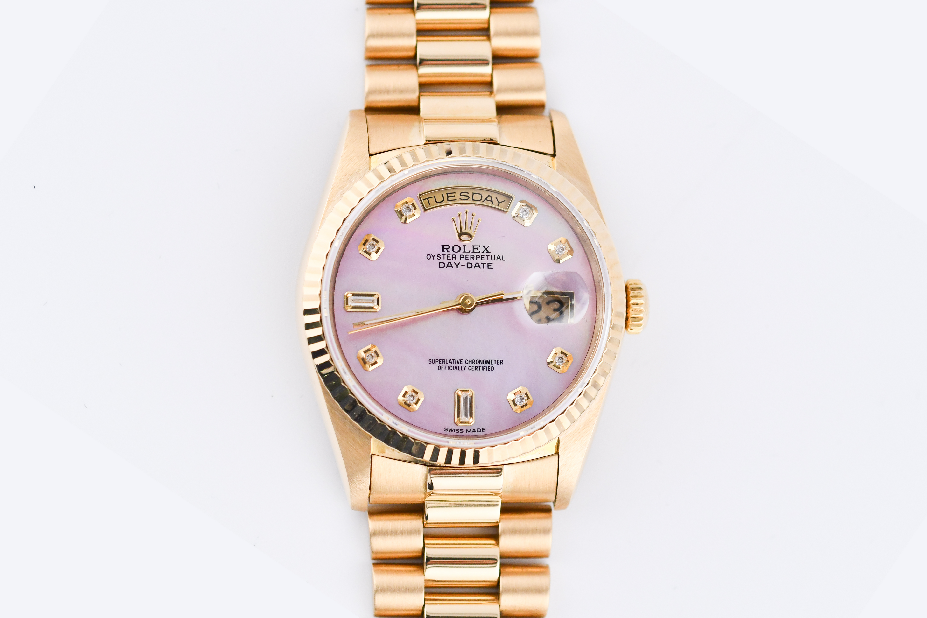 Gold wristwatch with a pink face on a white background