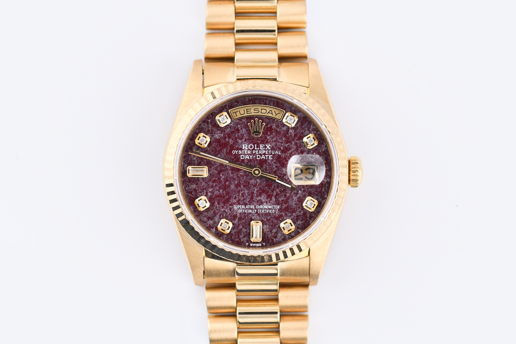 Gold watch with a maroon dial on a white background
