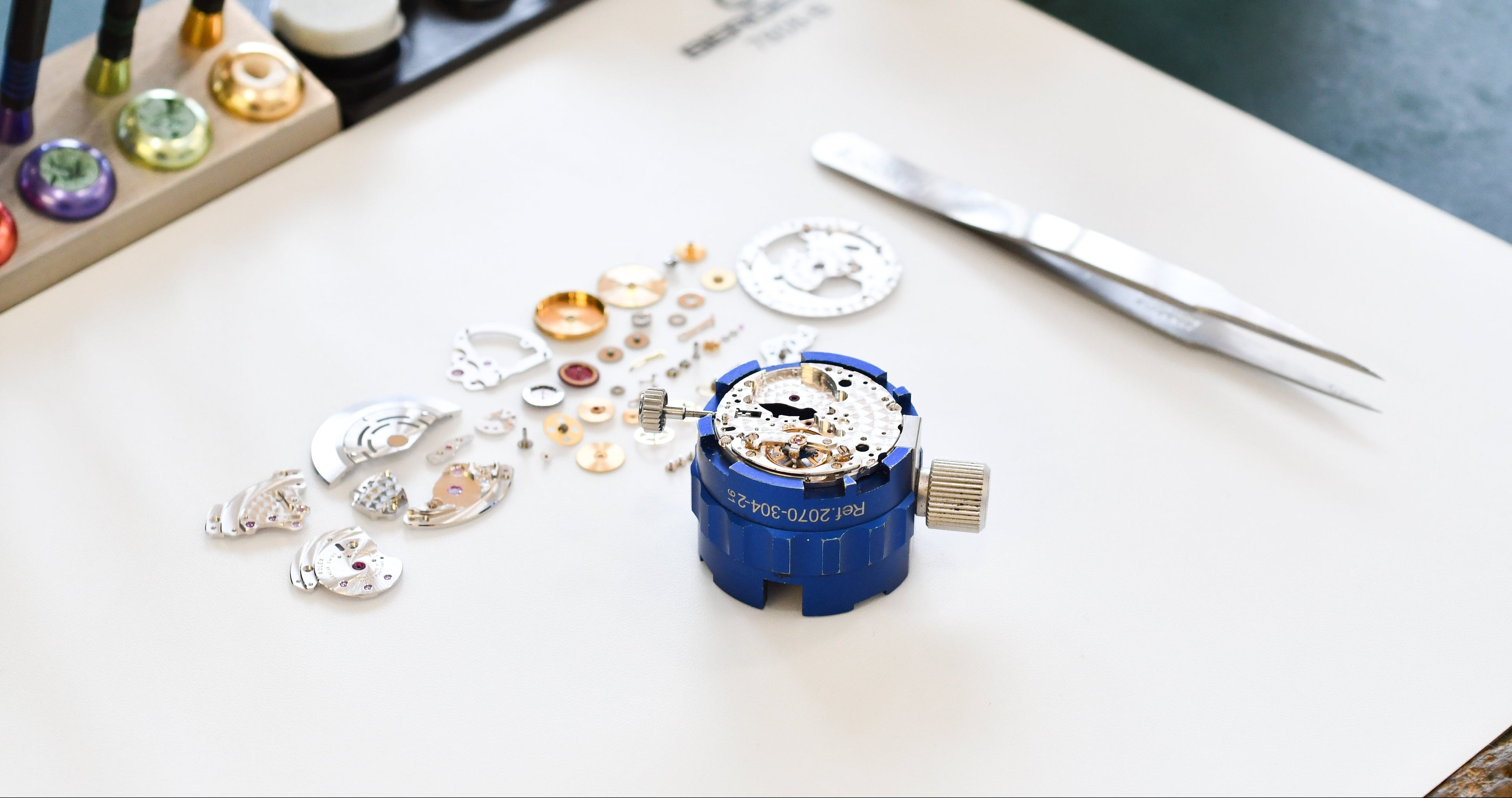 Watch mechanism on a white surface with tools and components